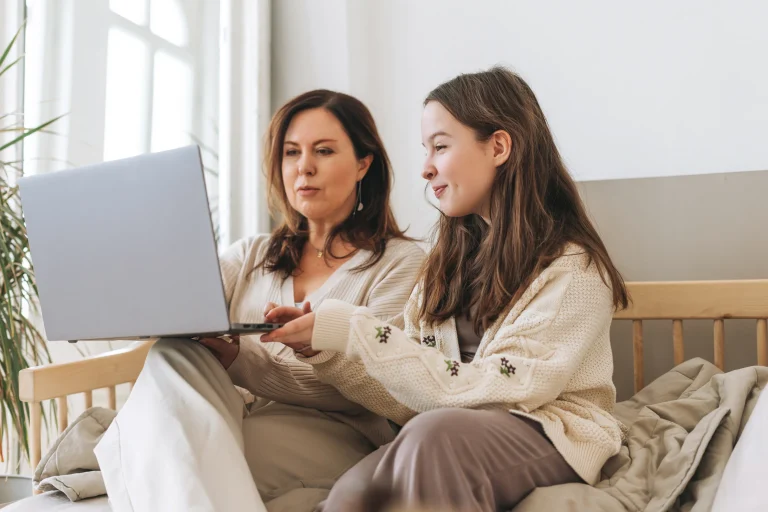 Madre conversa con su hija mientras revisan opciones de carreras universitarias en un computador.